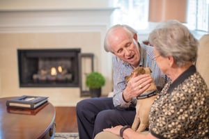 Couple on Couch petting dog in front of fire.