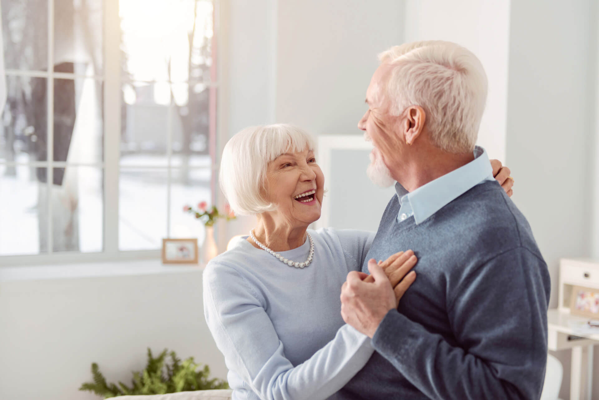 Senior couple embracing & smiling together inside their home