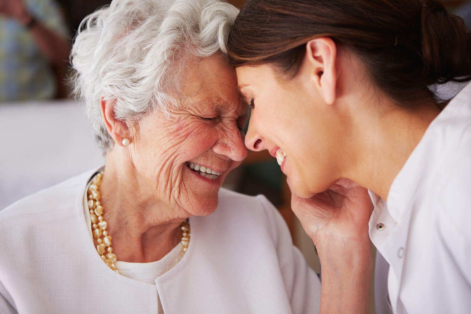 Senior woman laughing while embracing a young adult nurse