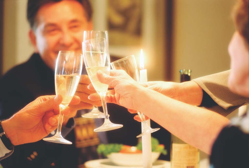 Extended arms of several adults, circled around a table, toasting with champagne glasses
