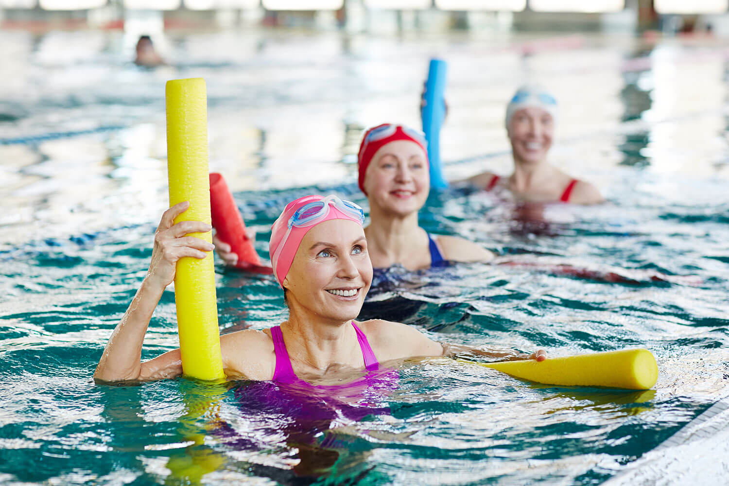 Older adult women in a pool with pool noodles doing water aerobics together