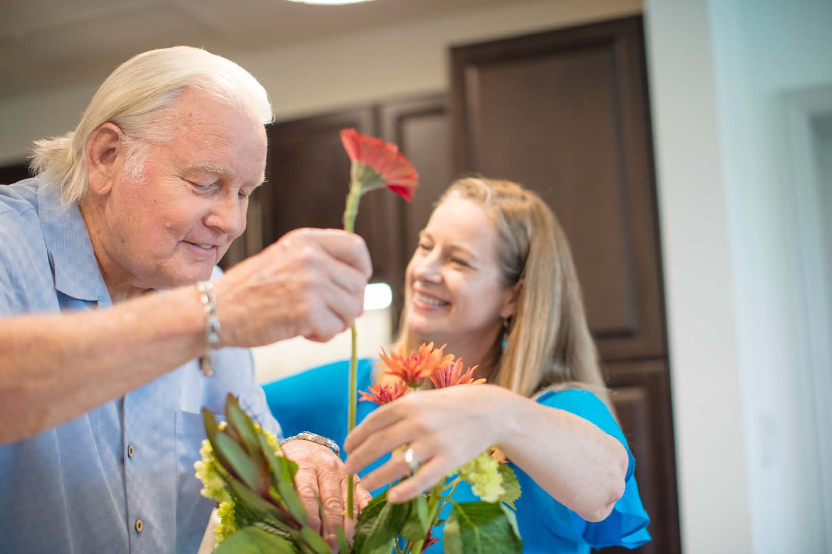 Senior man in kitchen area with adult child arranging a bouquet of red flowers